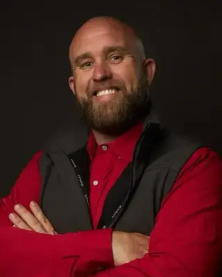 James Sendziak, founder of The Job Hog Construction, smiling with his arms crossed in a red shirt and gray vest
