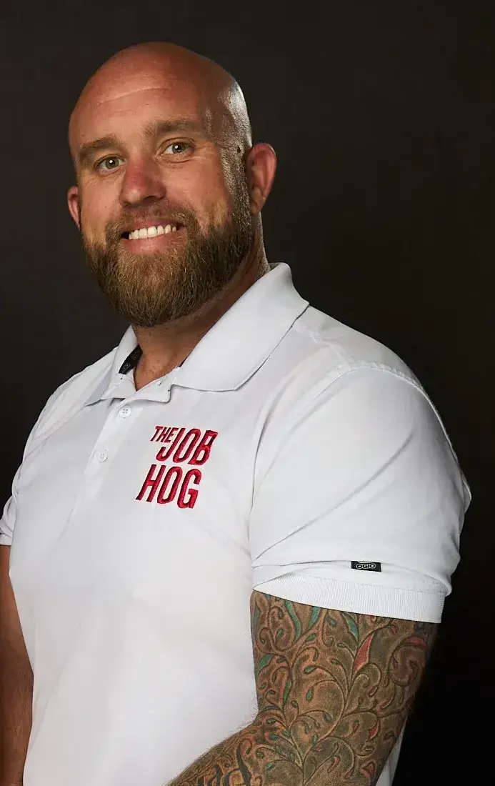 James Sendziak, owner of The Job Hog Construction, smiling in a white polo with the red Job Hog logo on the chest, studio portrait