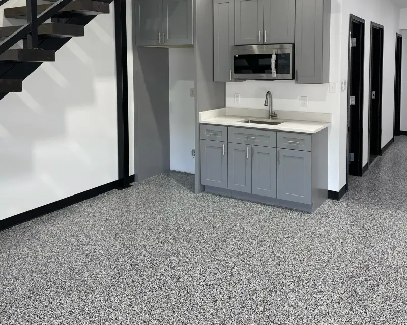 Gray flake epoxy floor in a finished shop with a gray-cabinet kitchenette, microwave and sink, a black steel staircase and black-framed doors