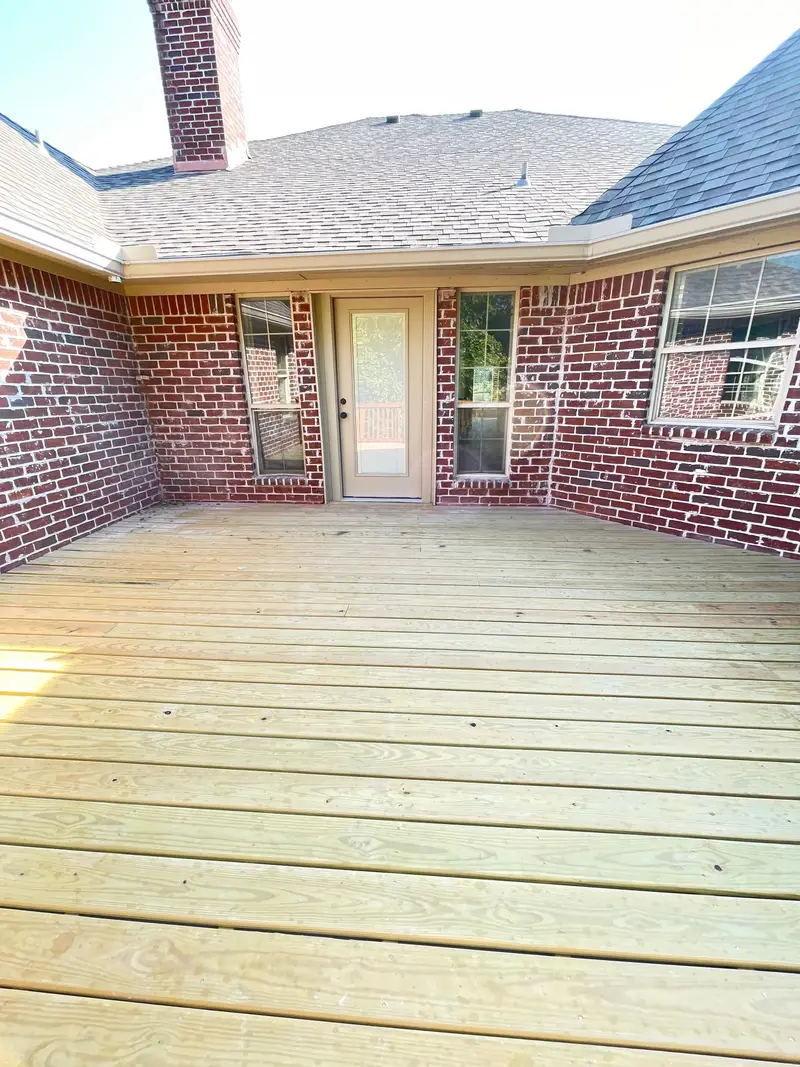 New pressure-treated timber deck across a brick home’s rear courtyard.