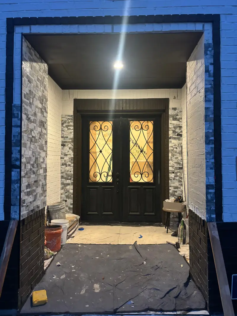 Black iron-and-glass double entry doors within a stone-clad entry surround during renovation.
