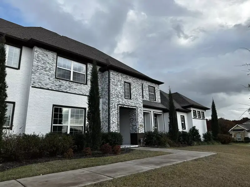 White-painted brick and stacked-stone facade on a two-story home with tall cypress trees.