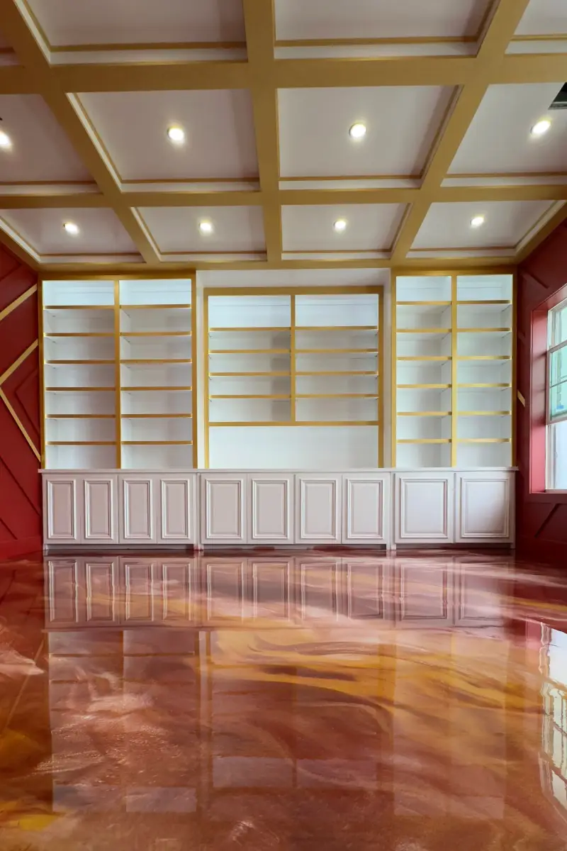 Room with a gold-trimmed coffered ceiling, white built-in shelving and a glossy copper metallic epoxy floor