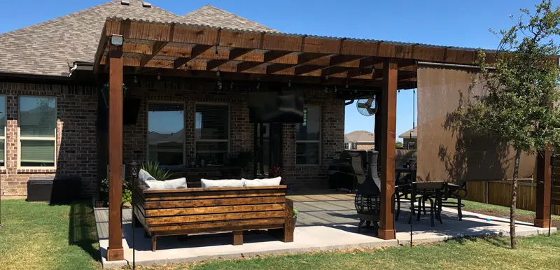 Cedar pergola at a brick home with built-in wood seating, patio furniture and adjacent lawn.